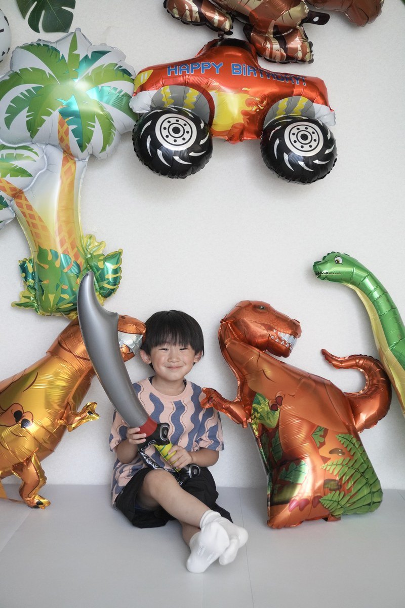 恐竜バルーンの前で剣を持つ子どもの誕生日写真