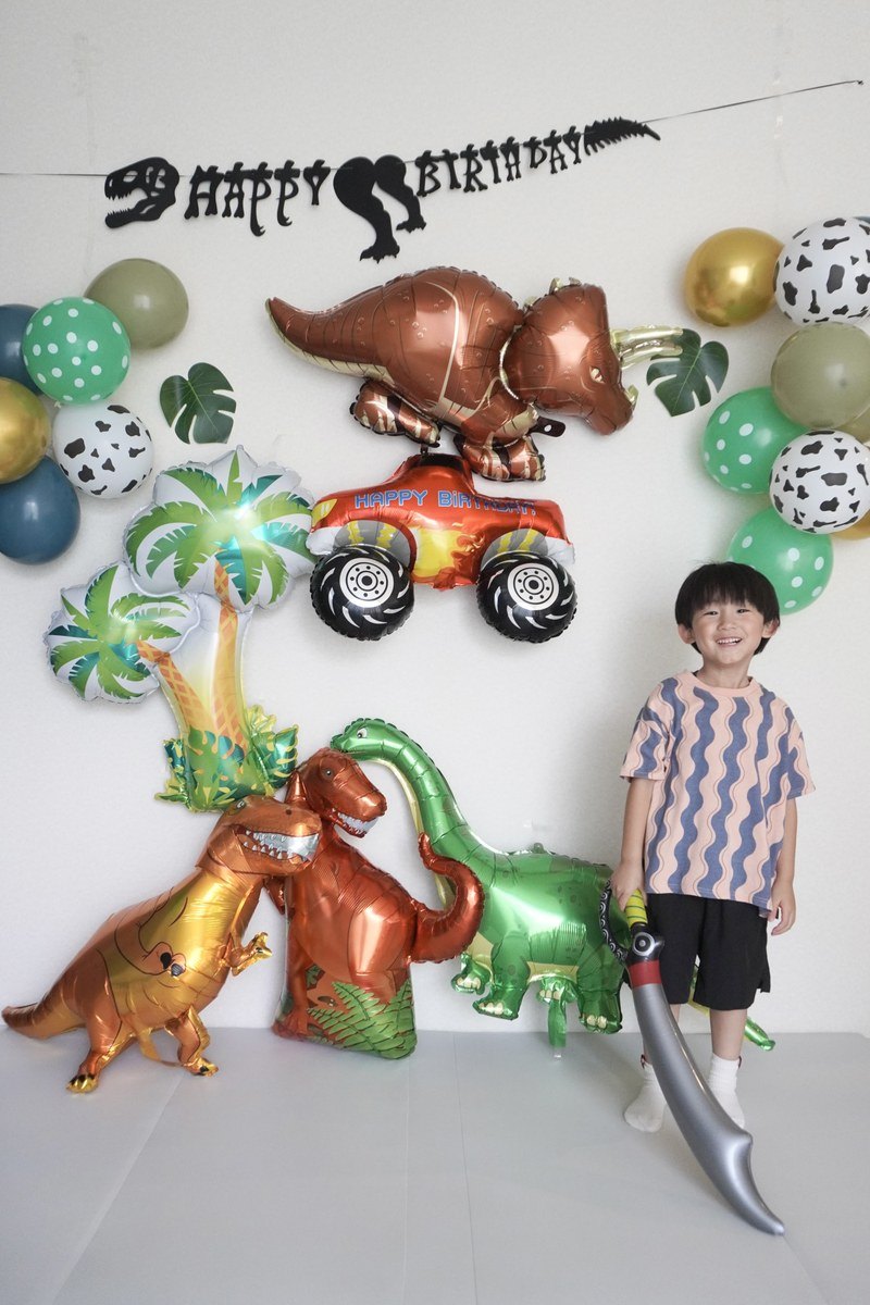 恐竜バルーンを壁いっぱいに飾った誕生日の実例。恐竜と一緒に写る子ども