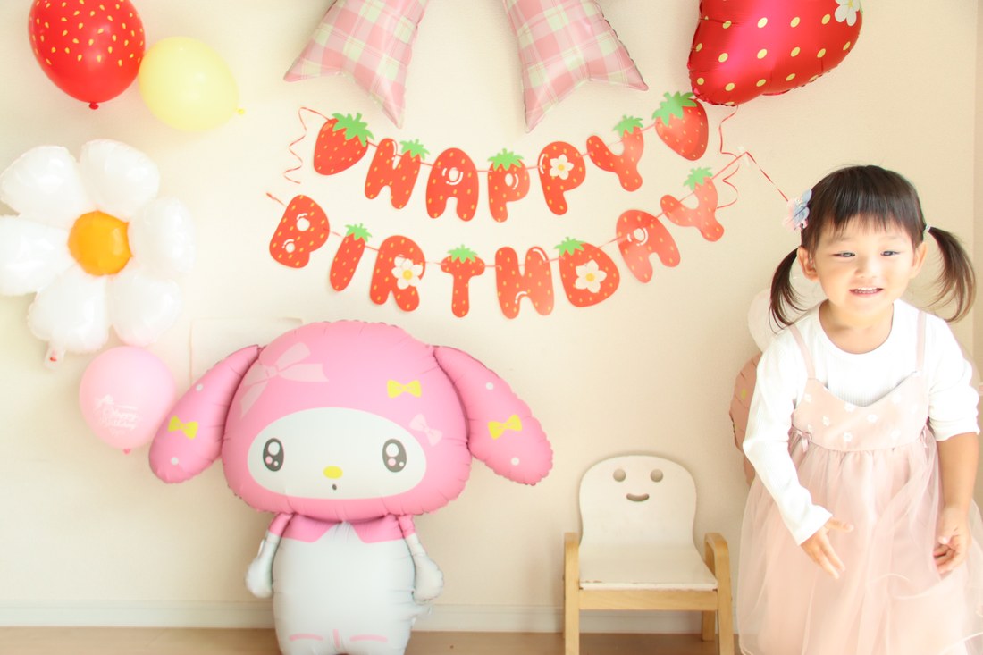 いちごマイメロのバルーンを飾った壁の前で、ピンクのお洋服でにっこり笑って立つお子さん（撮影：RIMIさん）