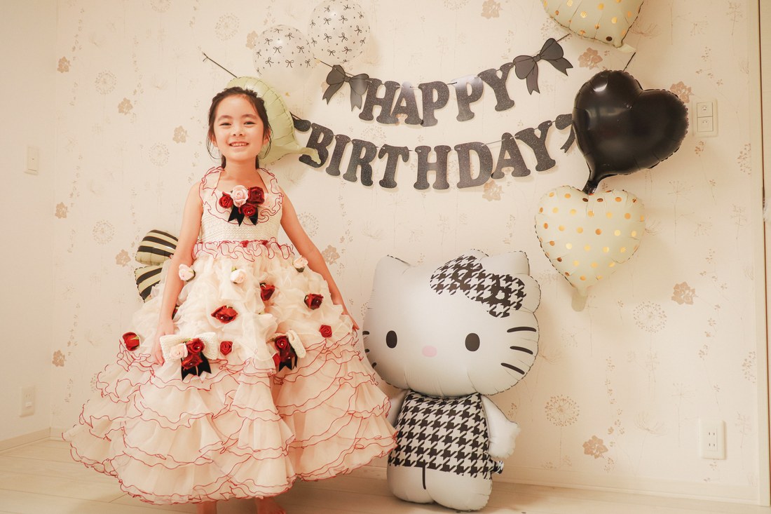 モノクロキティのバルーンを飾った壁の前で、赤いバラのドレスで立つお子さん（撮影：miraini_yumeoさん）