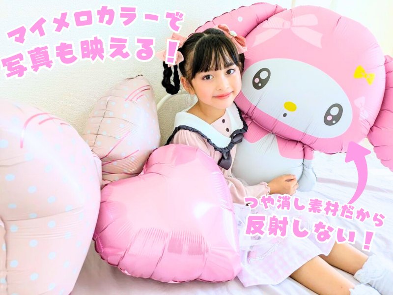 マイメロディのバルーンとピンクのハート、リボンのバルーンに囲まれて座るお子さん